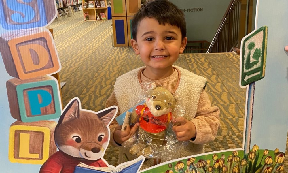 Young boy excited to receive his first library card and his Odi plush toy.