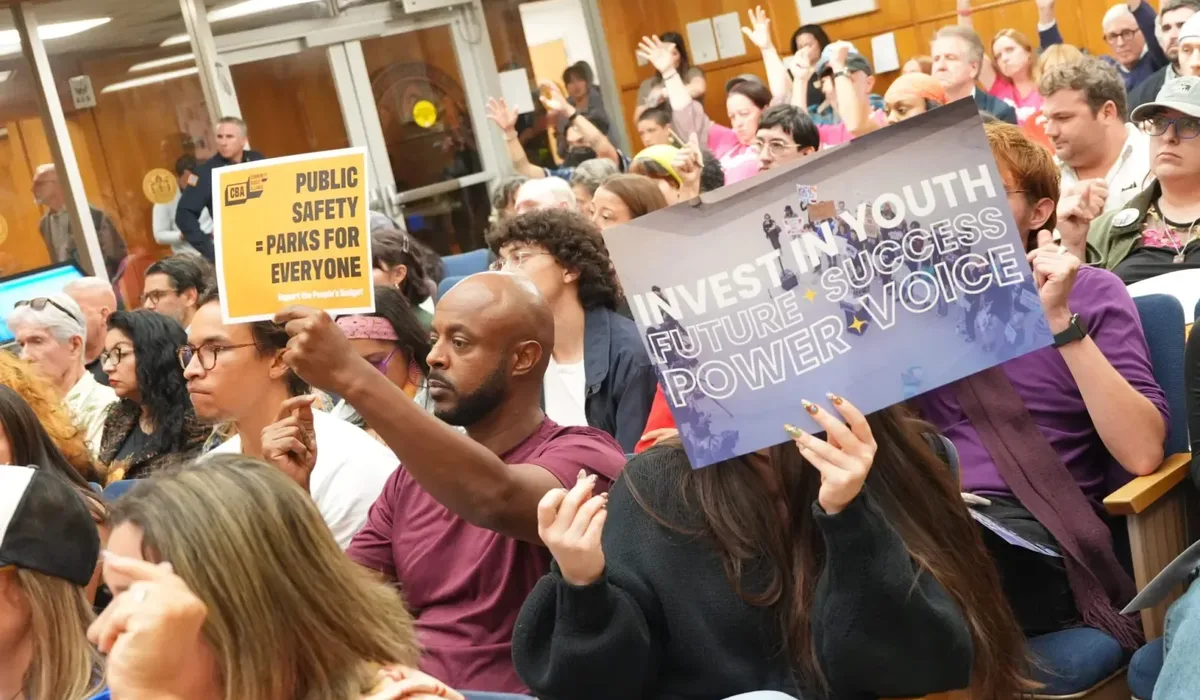 Petros Hagos, left, and Claire Snyder, right, hold posters during a budget hearing at City Hall on Wednesday, May 27, 2026, in San Diego. (Michael Ho / For The San Diego Union-Tribune)