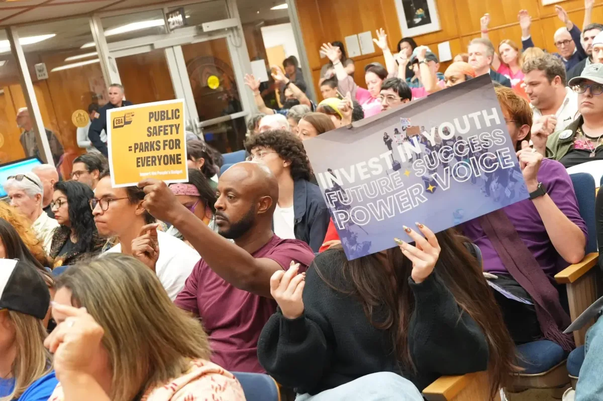 Petros Hagos, left, and Claire Snyder, right, hold posters during a budget hearing at City Hall on Wednesday, May 27, 2026, in San Diego. (Michael Ho / For The San Diego Union-Tribune)